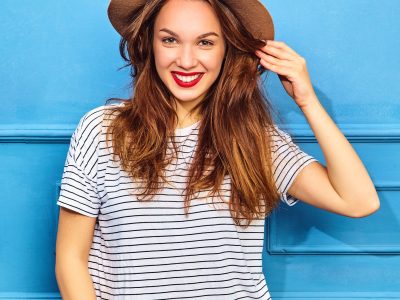 womens tshirt Young stylish girl model in casual summer clothes  and brown hat with red lips, posing near blue wall